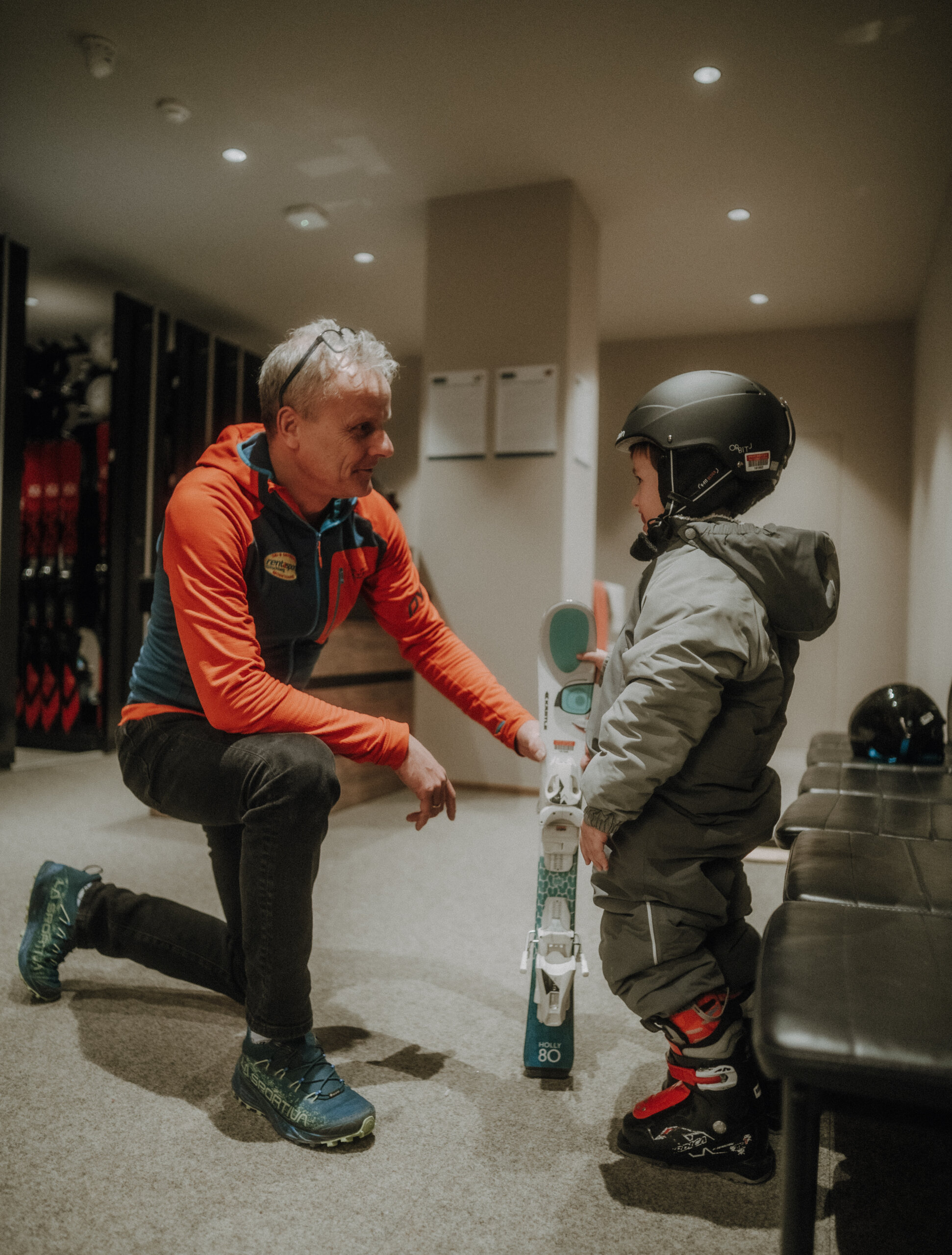 Kind mit Helm und Skianzu bekommt Ski zum Skifahren - Hotel Familiamus